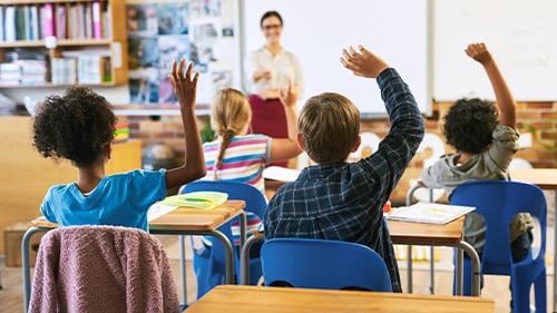 Teacher at the front of a classroom calling on students raising their hands
