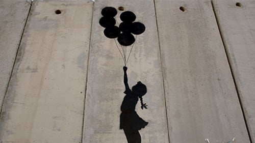 Banksy piece—black outline of girl holding ballons painted on wood slats