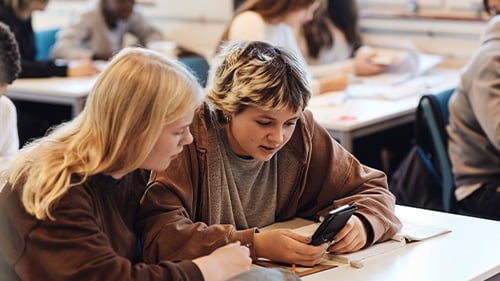 two high school students looking at text messages on a smartphone 
