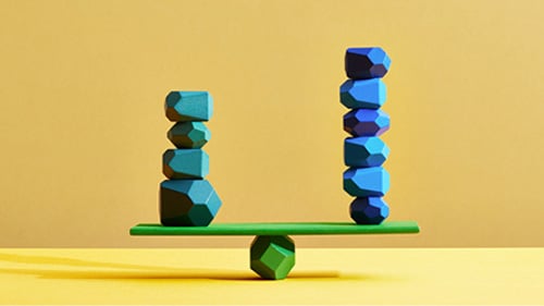 board balancing on a rock. On either side of the board balances two piles of rocks, the one on the left with more.
