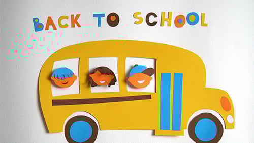 Cut out paper in the shape of a school bus and kids with cut out letters reading 