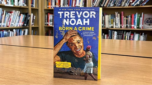 Cover of Born a Crime by Trevor Noah with library in the background