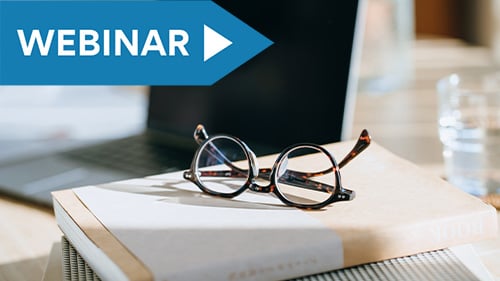 pair of reading glasses sits on book next to open laptop