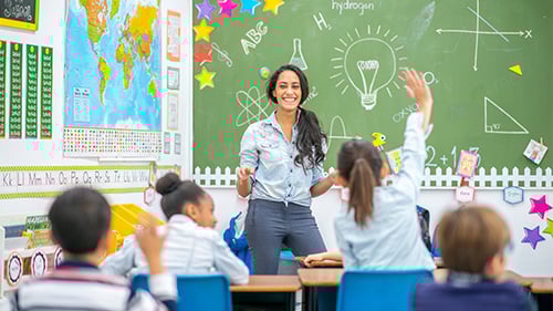 Teacher at front of classroom, student raises hand 