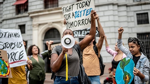 young protesters at a climate march hold up signs and fists. Many appear to be chanting. 
