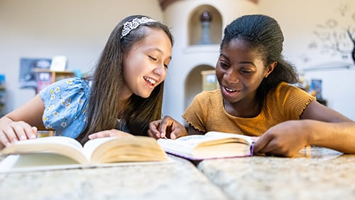two teenage girls reading books and smiling