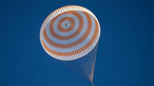 Orange and white striped parachute flying down from a clear blue sky 