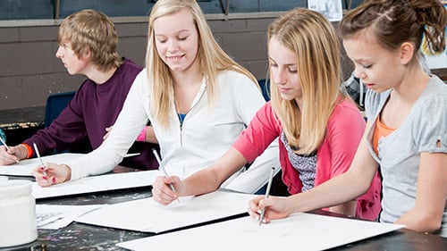 High school girls drawing on poster paper in a classroom