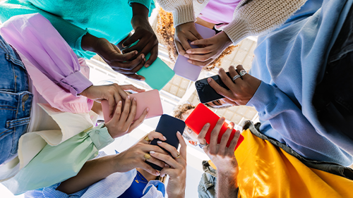 teens in colorful clothing stand in a circle using their smartphones