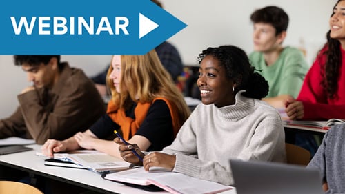 high school students looking forward in classroom. On the table in front of them are open books and laptops.