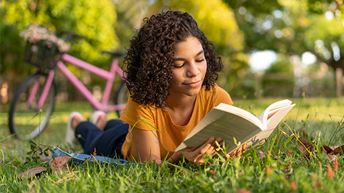 middle school girl reading a book outside and laying in the grass