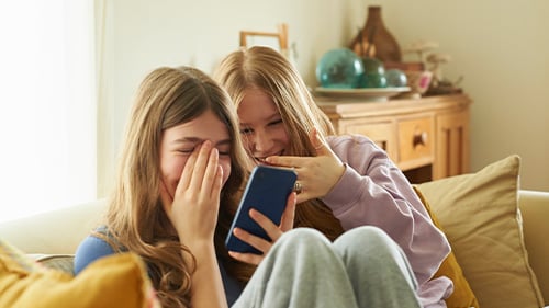 two teenage girls laughing at something on a smartphone