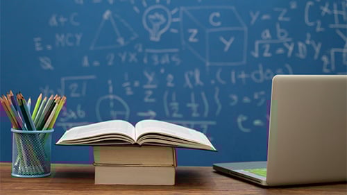 Stacks of books and laptop in front of blackboard with math problems on it