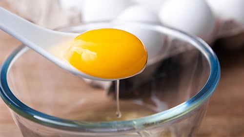 Spoon removing yolk from egg over glass bowl