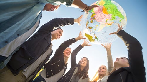 High school students put their hands on a plastic globe and smile