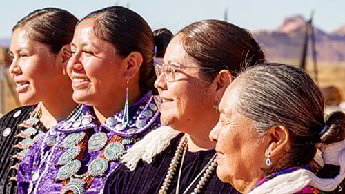 Four indigenous American women look out at scenery in traditional clothing. 