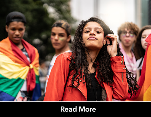 Group of teens of various ethnic, gender and sexual identities looking into camera and holding pride flags. 